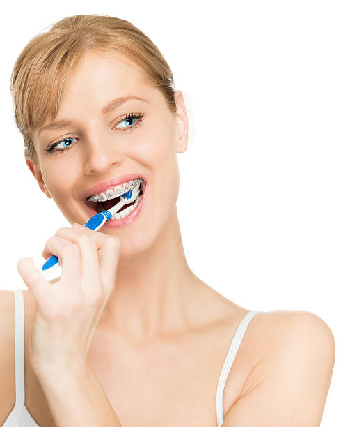 Attractive young woman with braces brushing teeth / copy space on right side